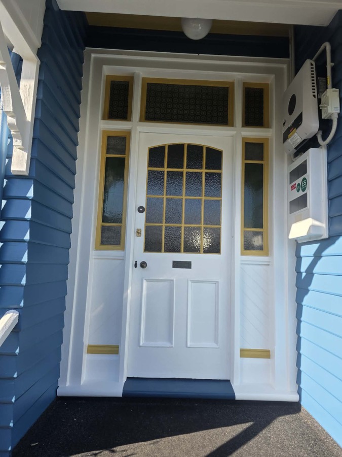 A white front door with yellow-trimmed glass panels on a blue bungalow